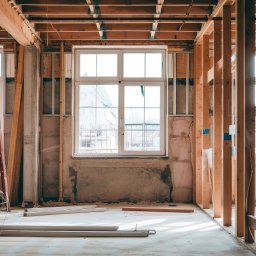 RENOVIO Sp. z o.o. - Wnętrze domu w trakcie budowy we Wrocławiu. Widoczne drewniane stelaże, okno i drabina. Surowy stan, przygotowanie do dalszych prac wykończeniowych.