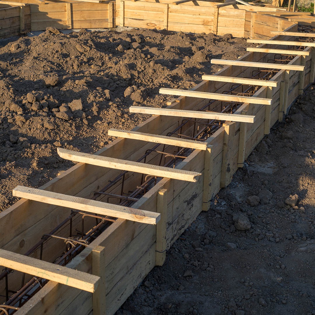 Szczegółowe ujęcie drewnianego szalunku zbrojonego stalą, przygotowanego do wylania fundamentów pod budowę domu. Widoczne elementy konstrukcji i ziemia.