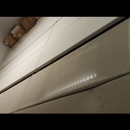 sandra pustelnik - Ściana z białych, błyszczących płytek ceramicznych, częściowo zabrudzonych, po remoncie. Widoczne ślady po czyszczeniu i kartony pod sufitem.