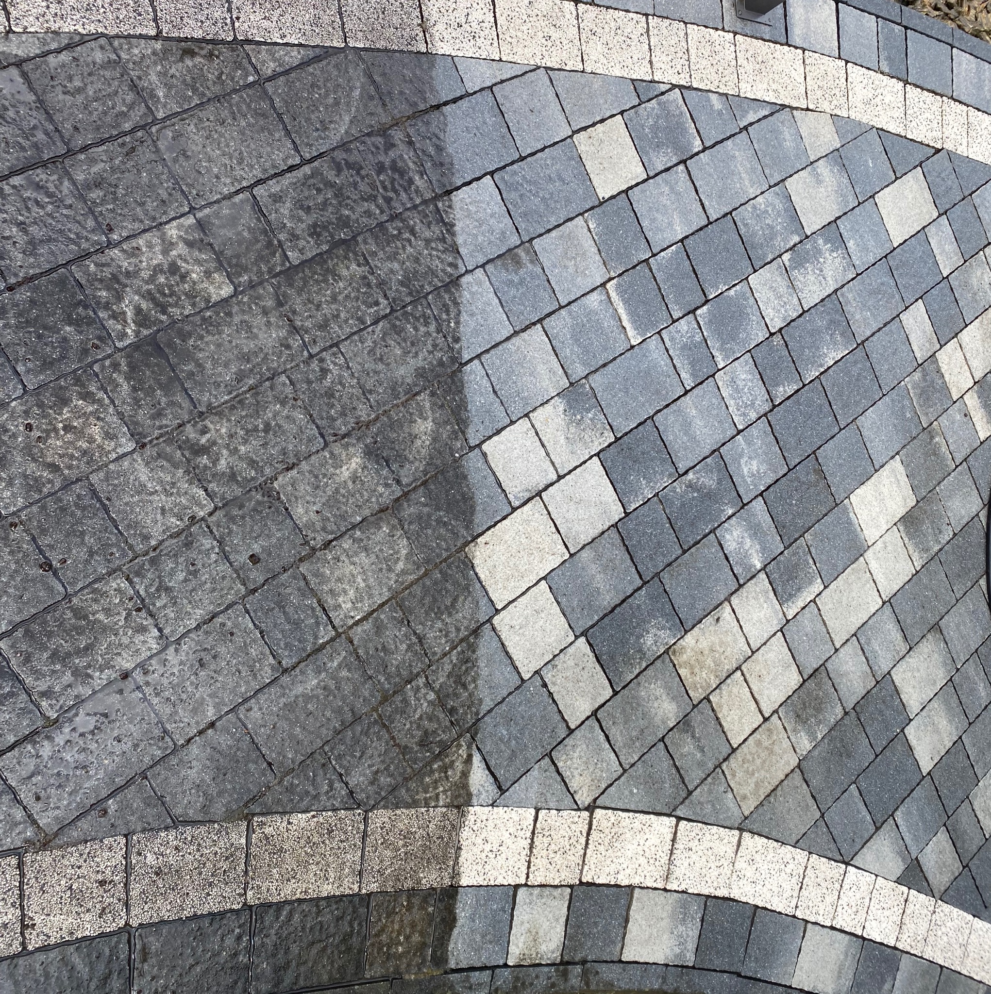 Częściowo umyta kostka brukowa w Świątnikach Górnych. Widoczny efekt czyszczenia: po lewej stronie brudna, po prawej czysta. Dekoracyjne obramowanie z jasnej kostki.