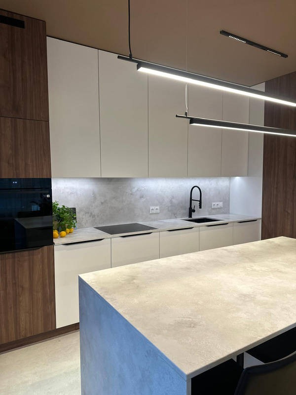 Nowoczesna kuchnia z wyspą, fronty w bieli i drewnie, betonowy backsplash, minimalistyczne oświetlenie liniowe i czarna armatura. Detale: cytryny i zieleń.