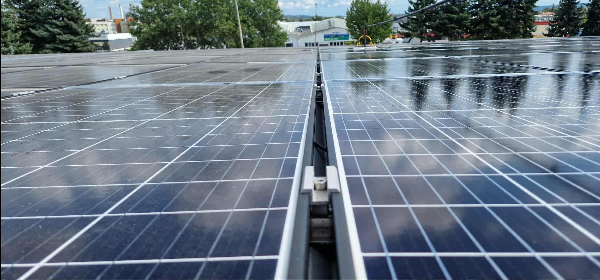 Umyte panele fotowoltaiczne na dachu budynku, widoczne odbicia nieba i chmur. Perspektywa z bliska, ukazująca detale konstrukcji i czystość powierzchni.