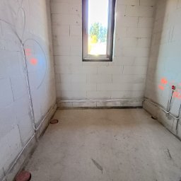 Piotr - Surowy pokój z instalacją elektryczną w ścianach z betonu komórkowego. Widoczne kable i puszki elektryczne, okno w tle. Etap prac przed tynkowaniem.