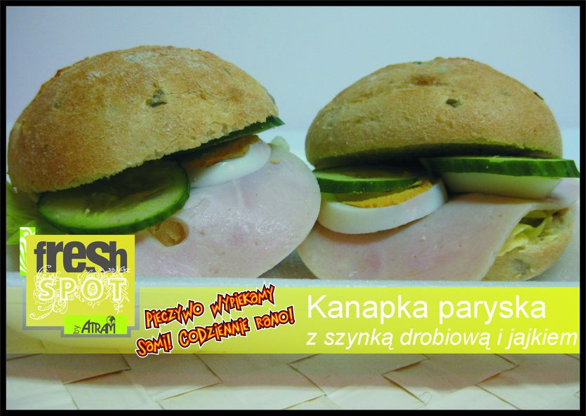 Dwie kanapki paryskie z szynką drobiową, jajkiem i ogórkiem, pieczywo z widocznymi nasionami, na żółtym tle z napisem reklamowym.