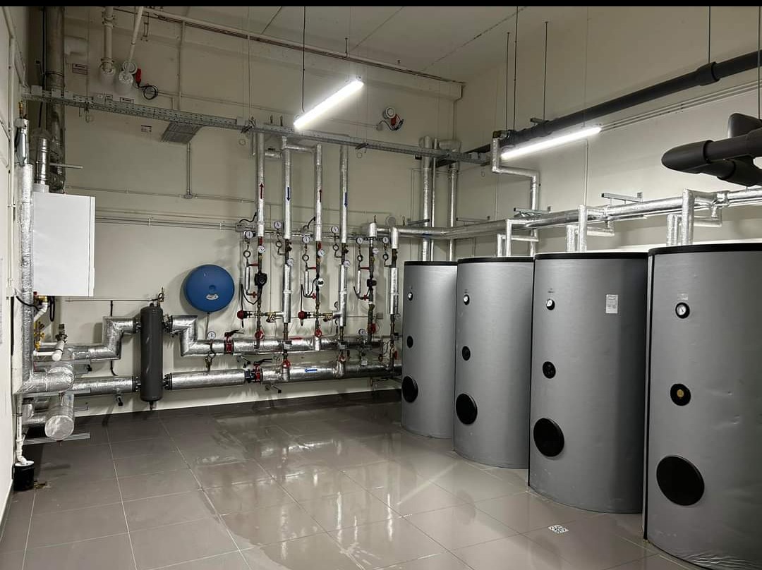 Kompleksowa kotłownia z czterema zbiornikami akumulacyjnymi i piecem w Chęcinach. Rury z zaworami i manometrami. Instalacja grzewcza z szarymi zbiornikami.