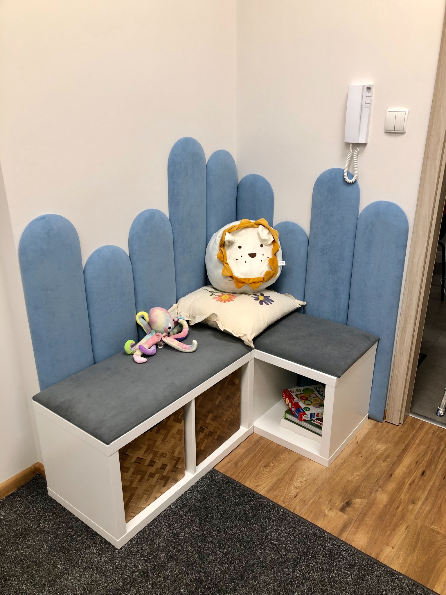 Kącik zabaw z niską zabudową, miękkimi siedziskami i pluszakami w gabinecie. Pastelowe kolory, przyjazna atmosfera, idealne miejsce dla dzieci.