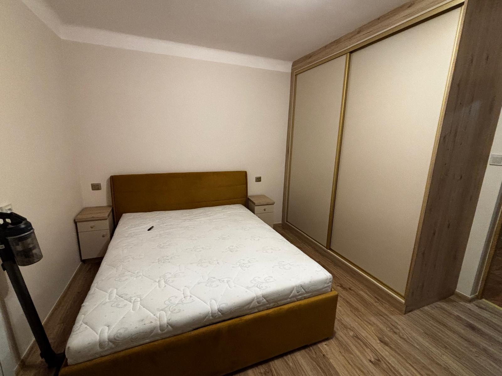 Nowoczesna sypialnia: złoty tapicerowany tapczan z materacem, szafki nocne i duża szafa przesuwna z jasnymi frontami, na podłodze panele. Widok na wnętrze.