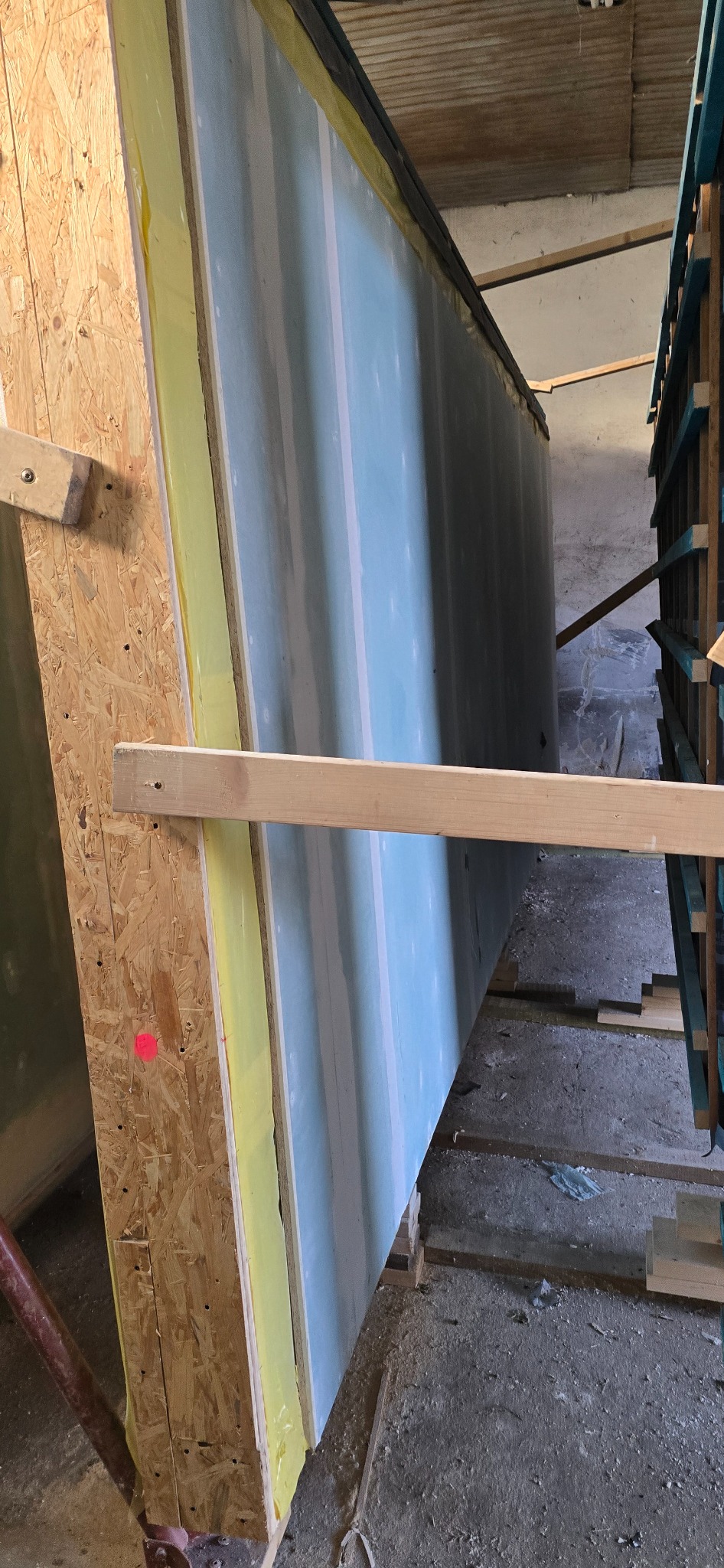 Wnętrze hali z elementami konstrukcyjnymi ścian, płyty gipsowe, drewniane podpory i izolacja. Widoczne detale montażu i przygotowania do dalszych prac budowlanych.