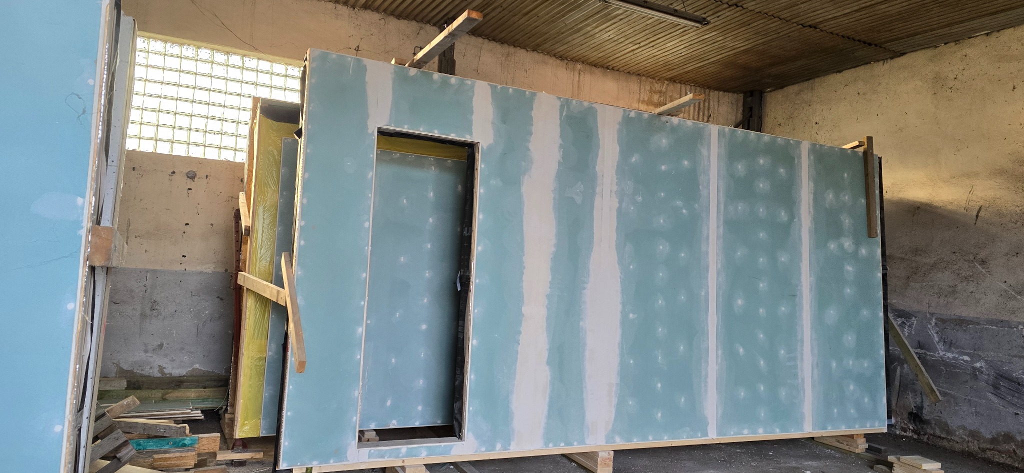 Gotowe elementy ścian z płyt gipsowo-kartonowych z otworem na drzwi, przygotowane do montażu w budynku. Widoczne szpachlowane łączenia.