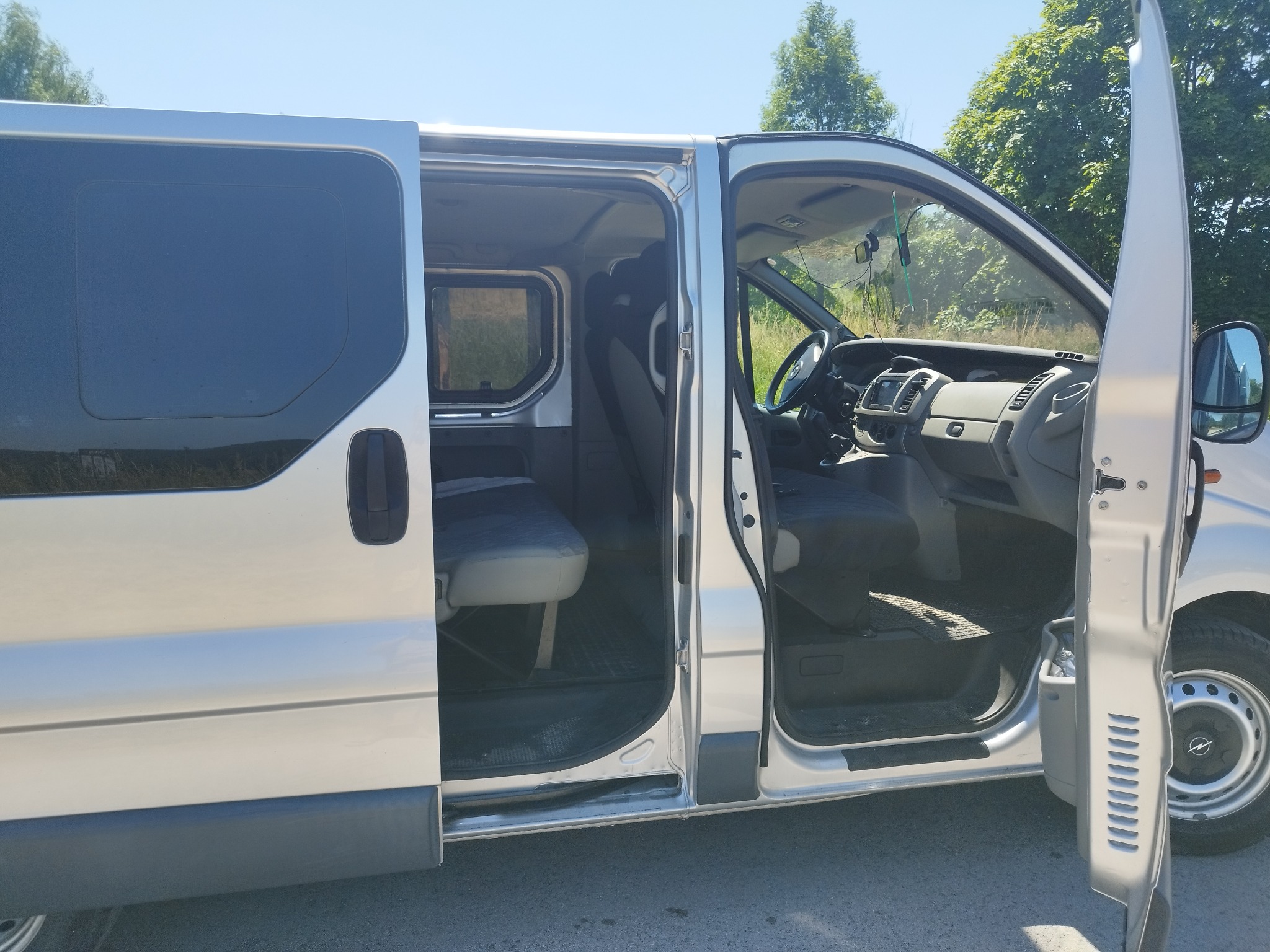 Srebrny van z otwartymi drzwiami bocznymi i przednimi, widoczne wnętrze pojazdu. Usługa przewozu osób.