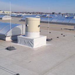 VSpark Volodymyr Semenikhin - Instalacja odgromowa na dachu budynku z świetlikami dachowymi, widoczne elementy systemu, przewody i uchwyty, na tle niebieskiego nieba.