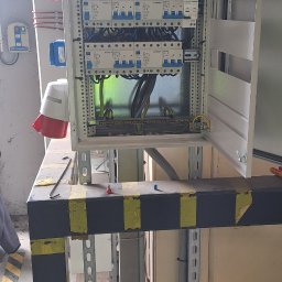 VSpark Volodymyr Semenikhin - Otwarta szafa elektryczna z zabezpieczeniami, widoczne okablowanie i gniazda siłowe. Szafa zamontowana na konstrukcji wsporczej z elementami ostrzegawczymi.