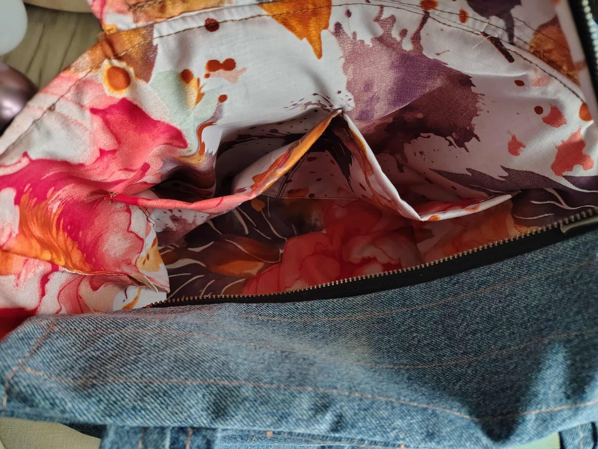 Otwarta torba jeansowa z kolorową, kwiecistą podszewką i kieszeniami wewnętrznymi, widoczny zamek błyskawiczny. Unikalny wzór podszewki.