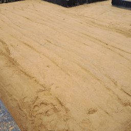 HA-BUD SPÓŁKA Z OGRANICZONĄ ODPOWIEDZIALNOŚCIĄ - Przygotowany teren pod wylewkę fundamentów z widocznymi śladami stóp i maszyn, otoczony szalunkiem. Piasek wyrównany, gotowy do dalszych prac budowlanych.