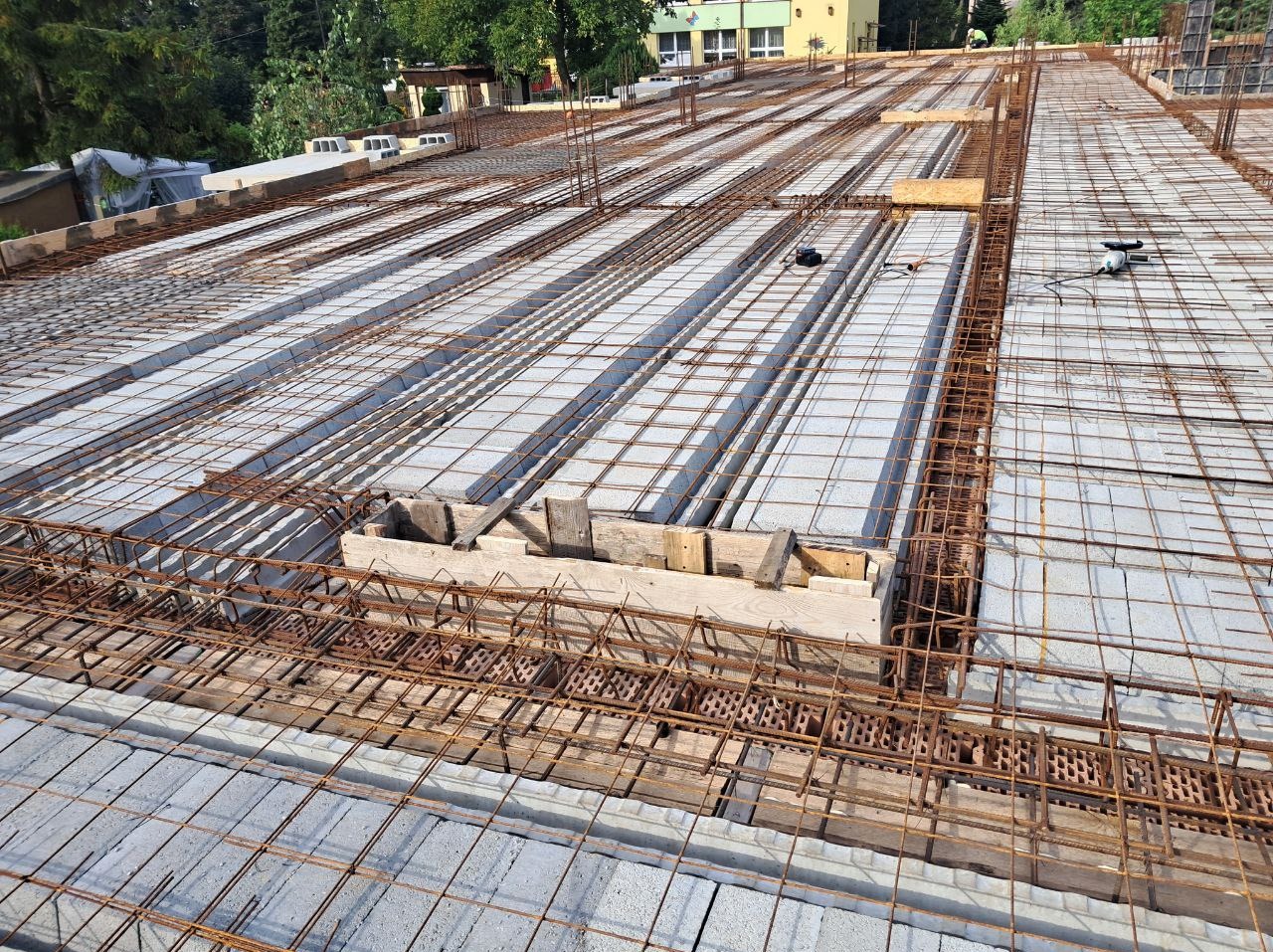 Konstrukcja stropu z szalunkiem i zbrojeniem, widok z góry. Elementy drewniane i stalowe tworzą regularny układ na tle betonowych bloczków.