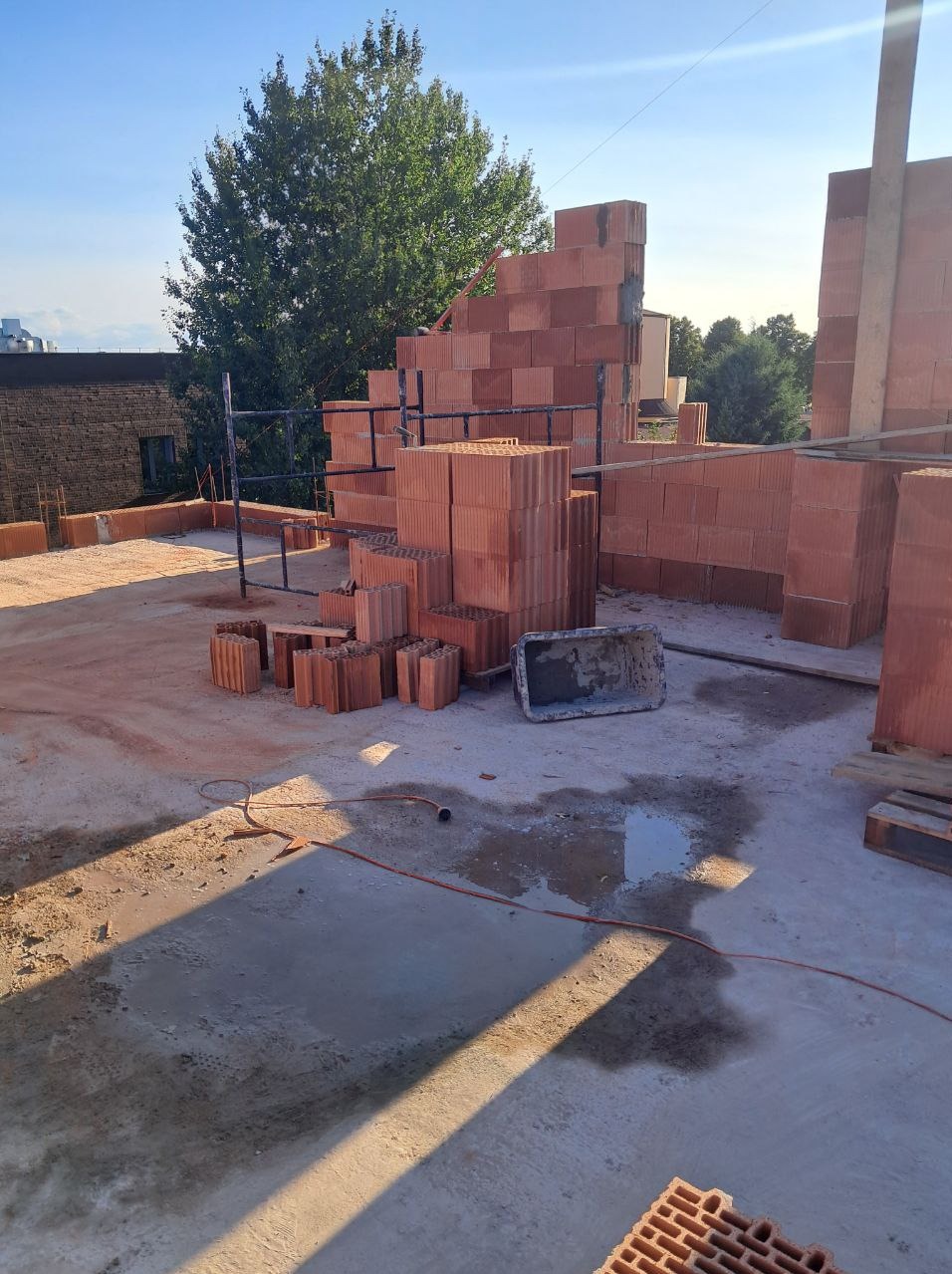Wznoszenie murów z czerwonej ceramiki na budowie. Widoczne pustaki, rusztowanie i narzędzia. Częściowo wzniesione ściany w słoneczny dzień.