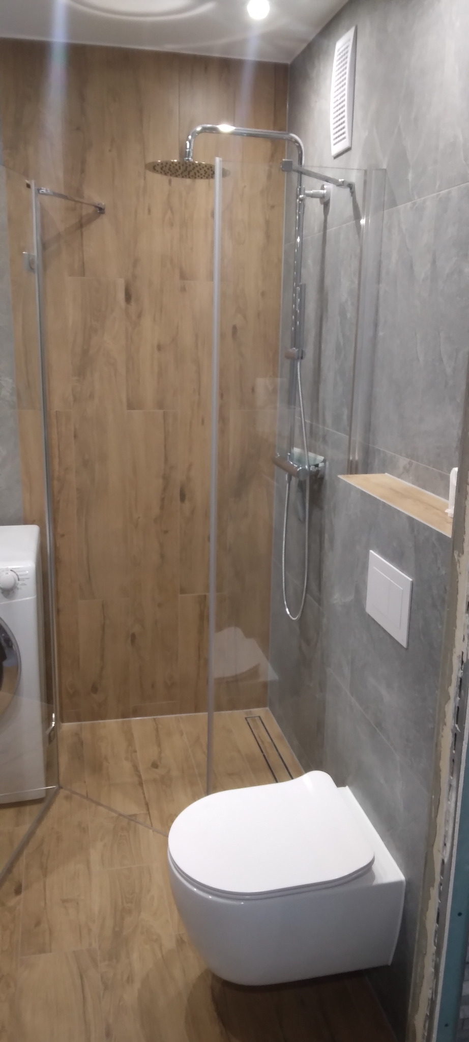 Nowoczesna kabina prysznicowa walk-in i podwieszana toaleta w wykończonej łazience w Wieliczce. Jasne płytki imitujące drewno i szare płytki na ścianach.