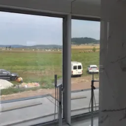 Panoramiczne okno z widokiem na krajobraz, w tle plac budowy z betoniarką. Nowoczesna łazienka z chromowaną armaturą częściowo widoczna.