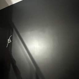 TWÓJ PARTNER GROUP SPÓŁKA Z OGRANICZONĄ ODPOWIEDZIALNOŚCIĄ - Ściana pomalowana na ciemny kolor z wystającymi przewodami elektrycznymi. Widoczne niedoskonałości malowania, oświetlenie boczne.