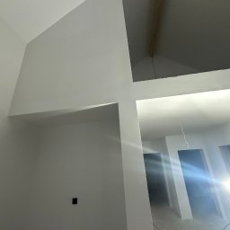 TWÓJ PARTNER GROUP SPÓŁKA Z OGRANICZONĄ ODPOWIEDZIALNOŚCIĄ - Białe ściany po malowaniu w nowym domu z elementami konstrukcyjnymi stropu i instalacją elektryczną. Widok na korytarz i drzwi.