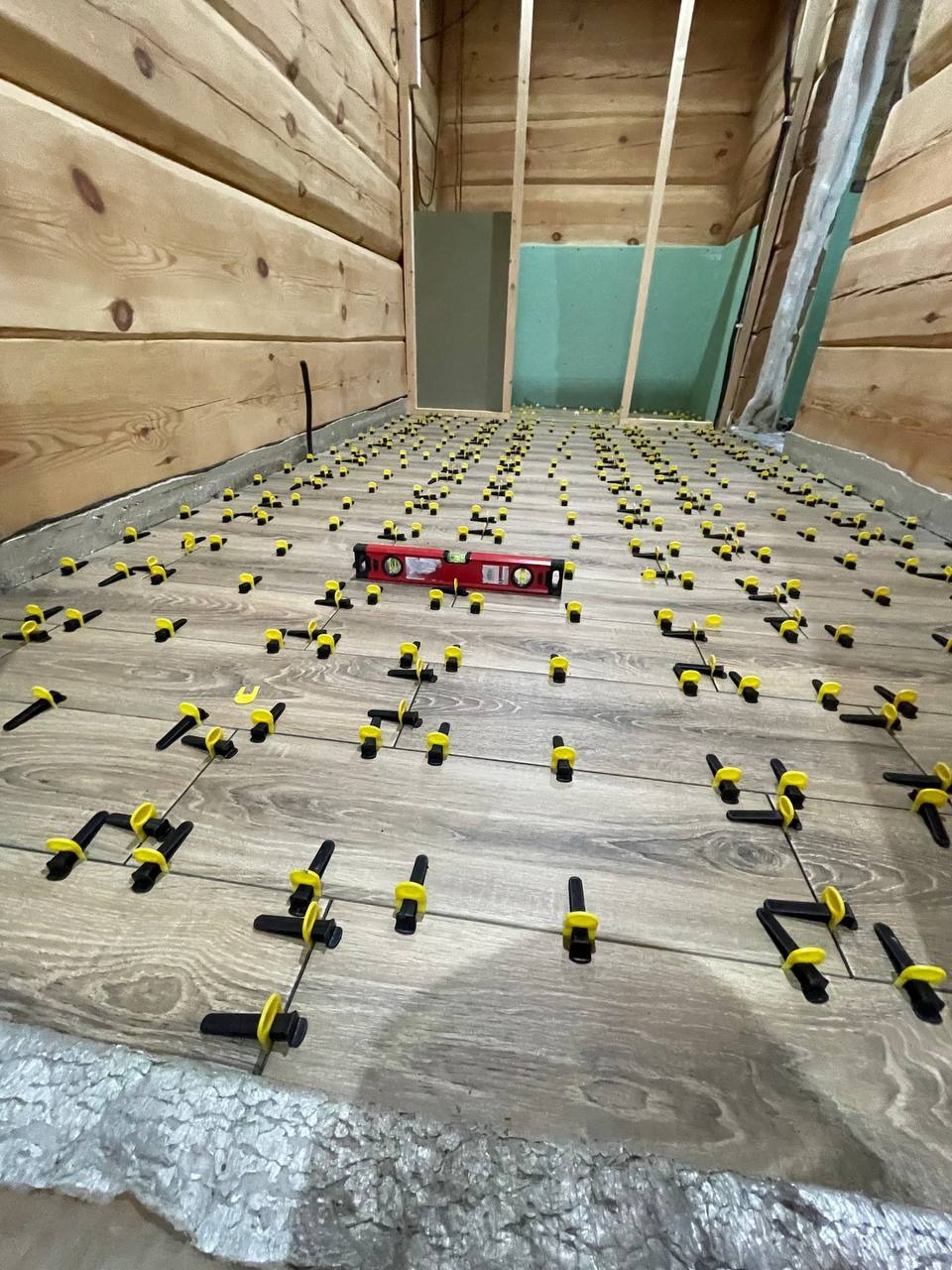 Układanie paneli podłogowych w drewnianym wnętrzu, z użyciem poziomicy i klipsów dystansowych. Widoczna izolacja pod panele.