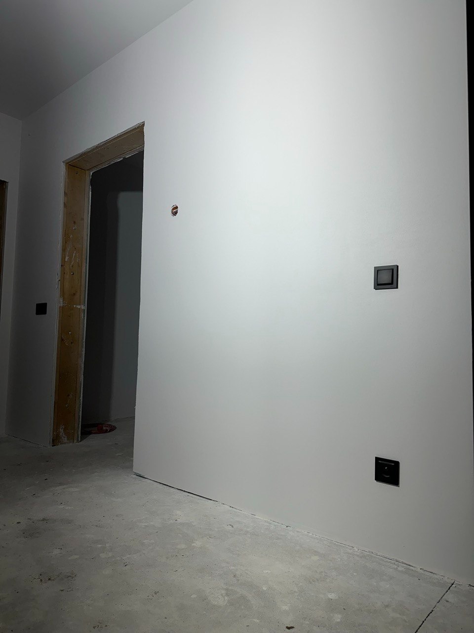 Świeżo pomalowane, białe ściany z czarnymi włącznikami, surowa ościeżnica i betonowa podłoga w nowym wnętrzu. Widoczny otwór po gniazdku.