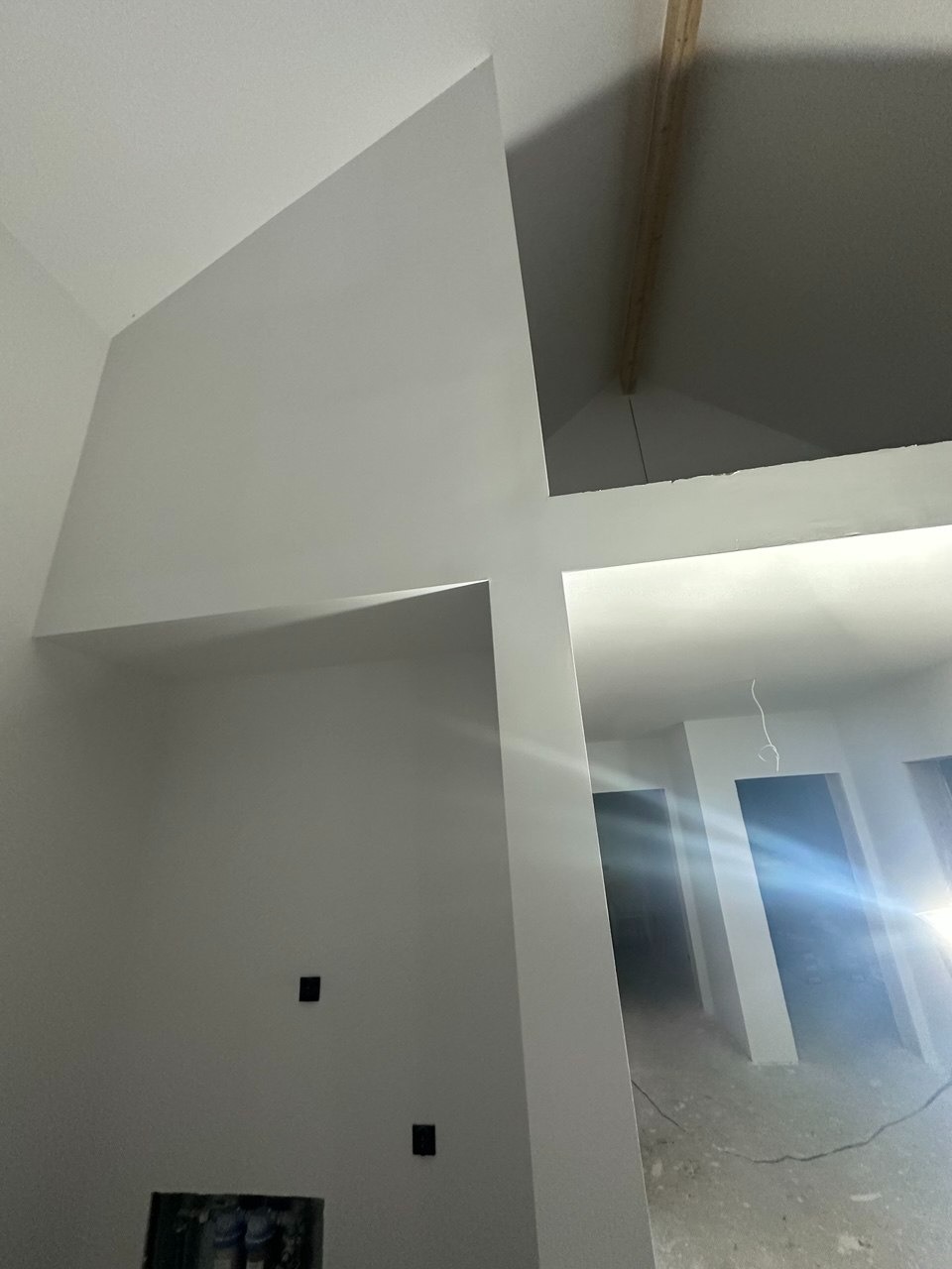 Białe ściany po malowaniu w nowym domu z elementami konstrukcyjnymi stropu i instalacją elektryczną. Widok na korytarz i drzwi.