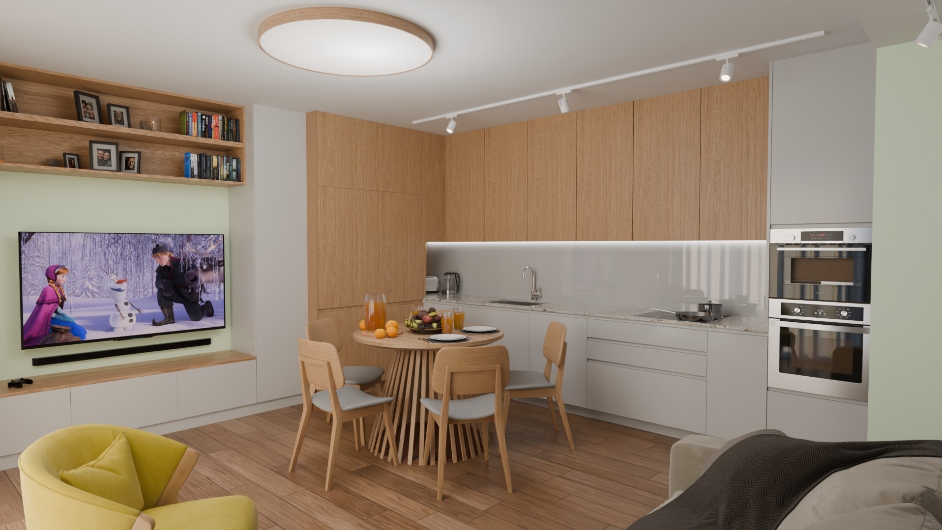Jasna kuchnia z drewnianymi szafkami, okrągłym stołem i krzesłami. Na ścianie telewizor z bajką 'Kraina Lodu'. Nowoczesne oświetlenie sufitowe.