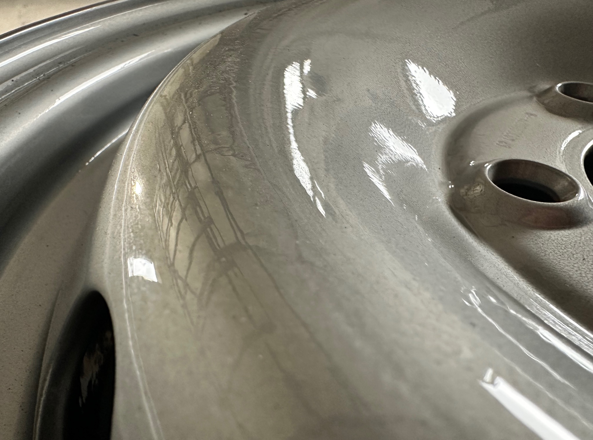 Błyszczący, srebrny fragment felgi samochodowej z otworami, sfotografowany pod kątem, ukazujący gładką powierzchnię po obróbce.