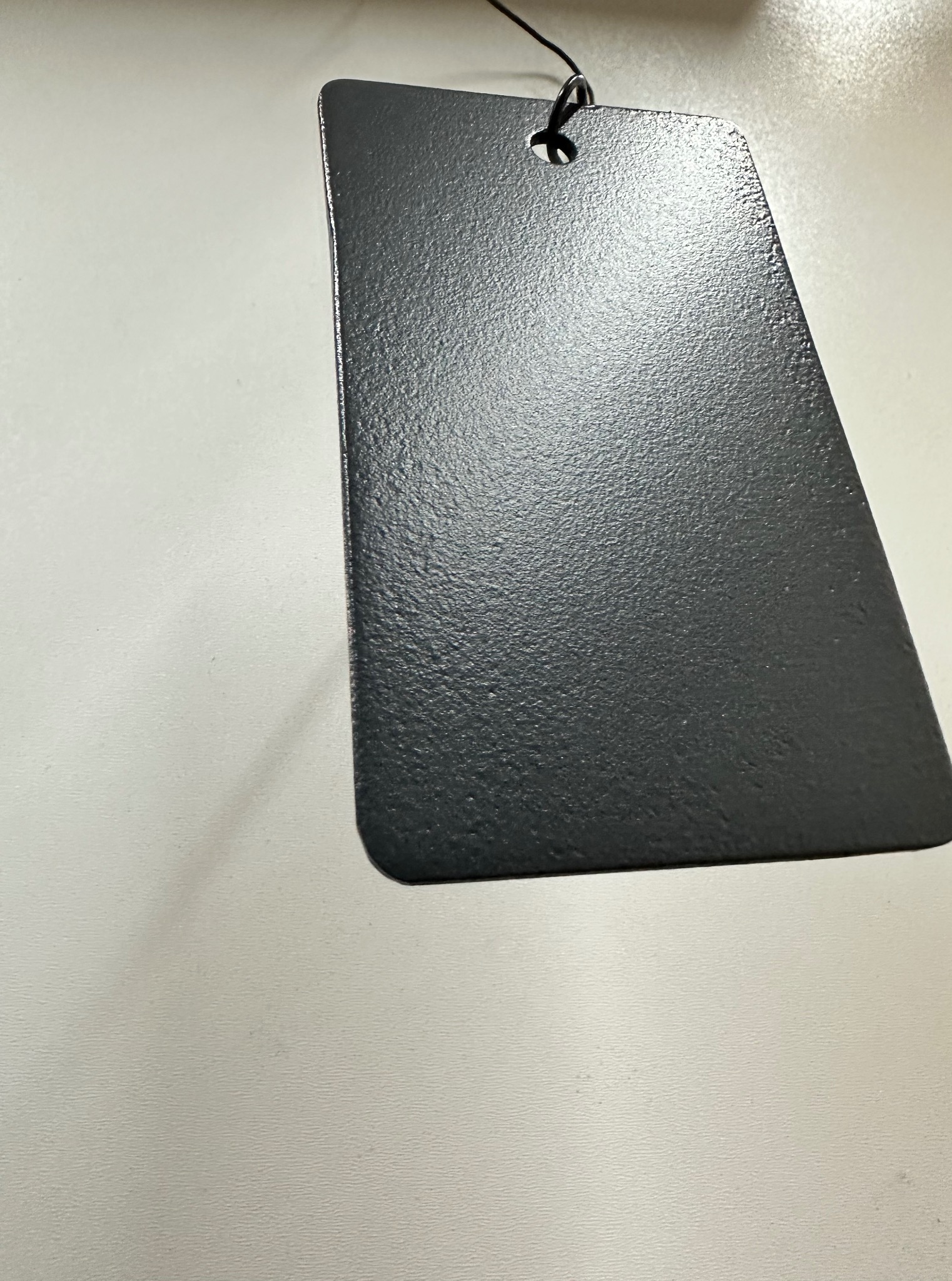 Czarny, metalowy element z otworem, zawieszony na lince, prezentujący chropowatą fakturę powierzchni po obróbce.