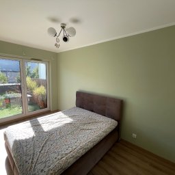 SunSet - Pokój po malowaniu: zielone ściany, brązowe łóżko, widok na ogród przez okno balkonowe. Świeżo pomalowane ściany w odcieniu zieleni.