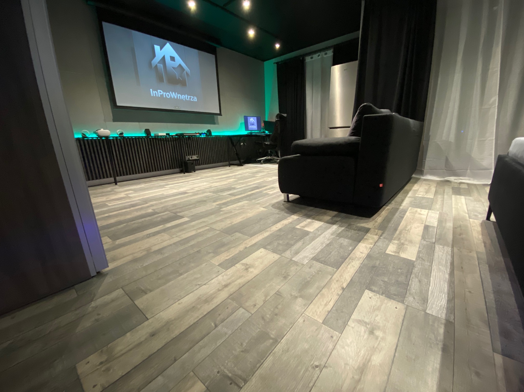 Nowoczesne wnętrze z drewnopodobną podłogą, projektorem wyświetlającym logo firmy InProWnetrza oraz oświetleniem LED, emanujące minimalistycznym stylem.