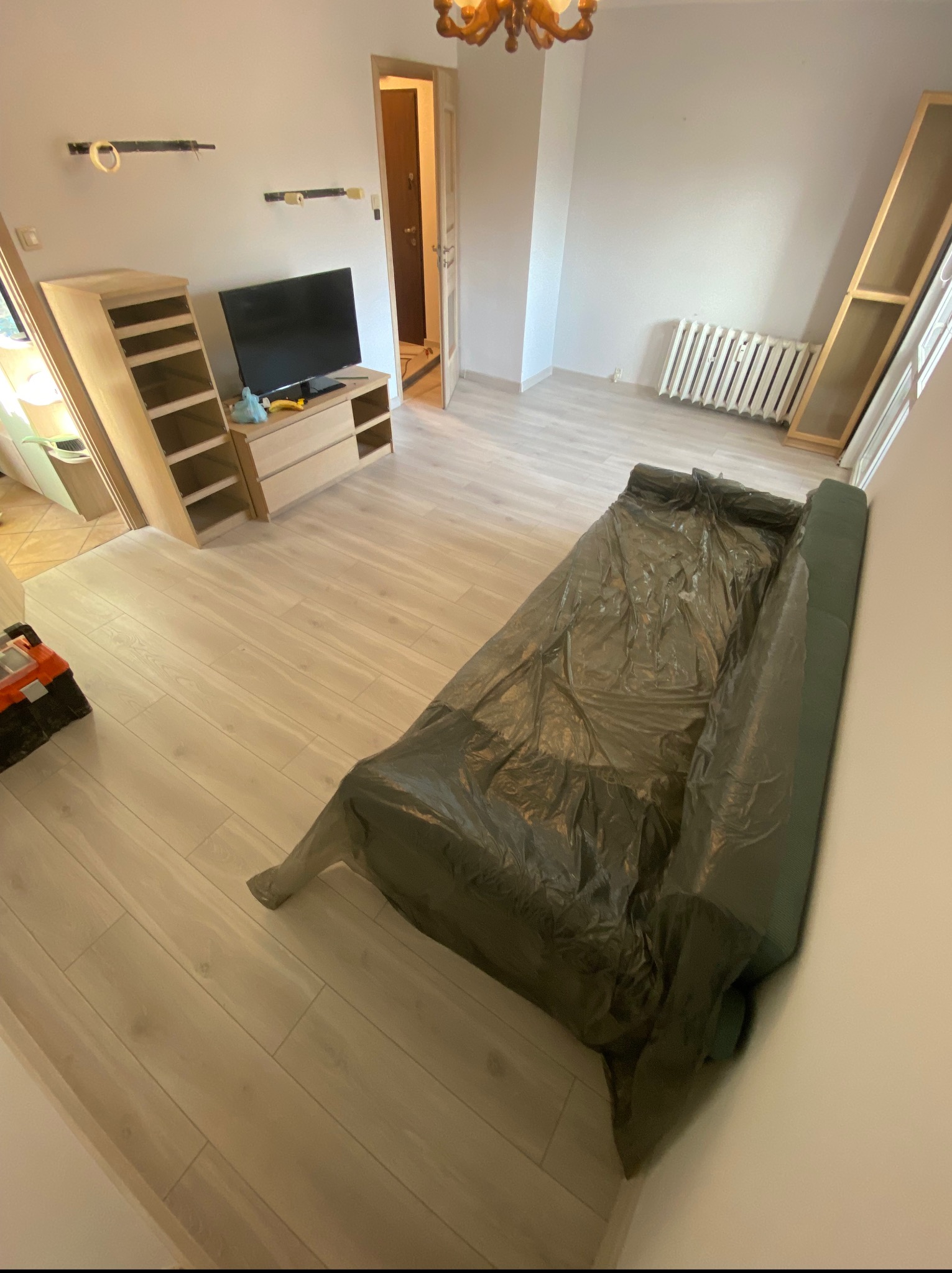 Pokój w trakcie przygotowań do prac wykończeniowych. Podłoga zabezpieczona folią, widoczne meble w trakcie montażu i narzędzia.