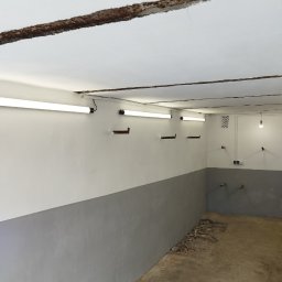 Paw-Bud-Trans Paweł Górski - Wnętrze piwnicy po malowaniu: szara lamperia, białe ściany powyżej, widoczne lampy fluorescencyjne i ślady po instalacjach na ścianach.