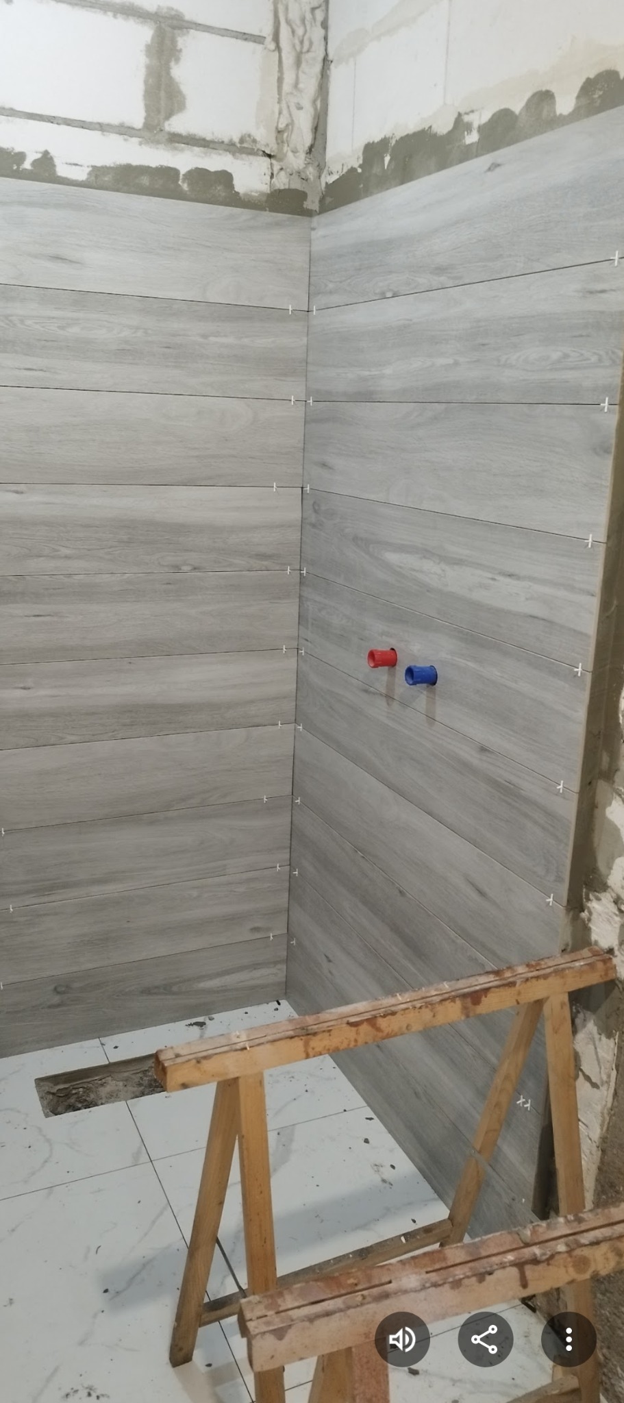 Wykończenie łazienki: szare płytki imitujące drewno ułożone poziomo na ścianach, z widocznymi krzyżykami dystansowymi i wystającymi rurami z instalacji wodnej.