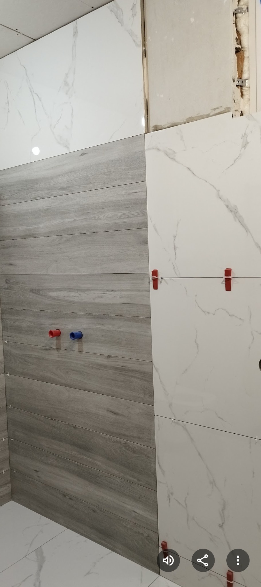 Ściana z płytek imitujących drewno i marmur, z widocznymi elementami montażowymi i otworami na rury. Układanie płytek w trakcie realizacji.