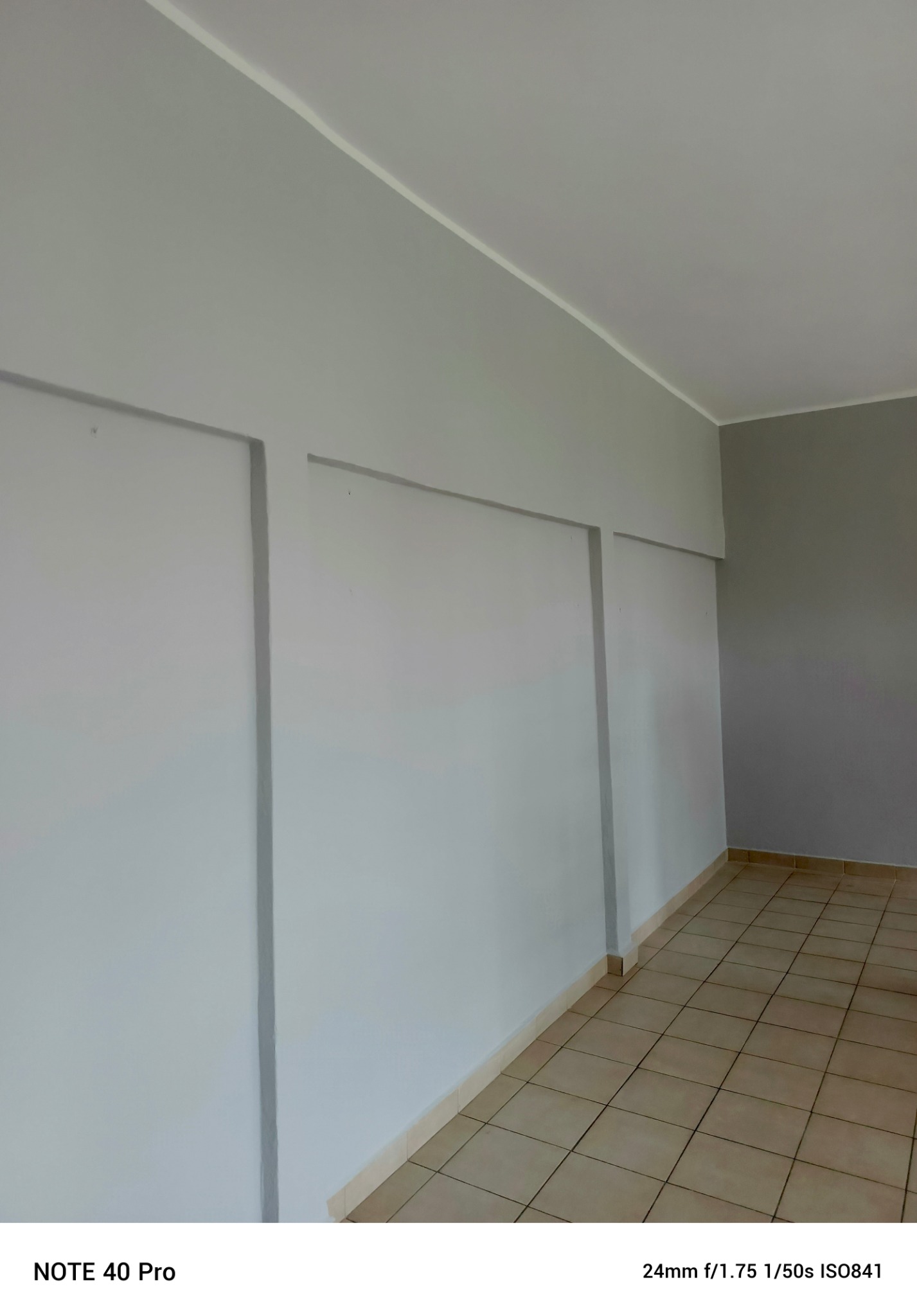 Wnętrze pokoju po malowaniu ścian na dwa odcienie szarości, z widoczną podłogą wyłożoną płytkami w odcieniach beżu. Ściany pomalowane w pionowe pasy.