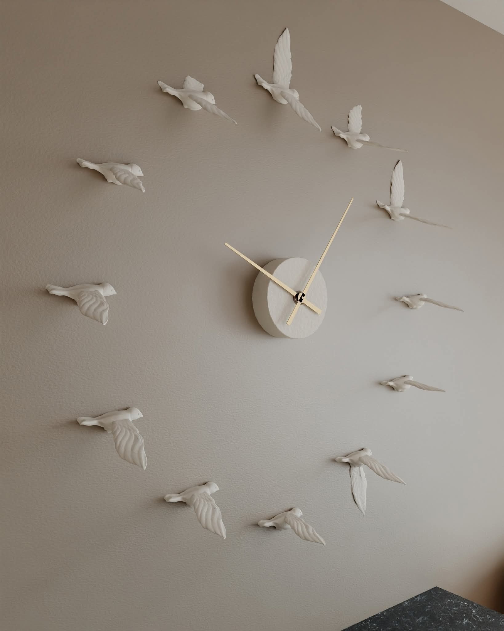 Beżowa ściana z oryginalnym zegarem: okrągła tarcza i złote wskazówki otoczone białymi, ceramicznymi ptakami w locie. Dekoracja wnętrza w minimalistycznym stylu.