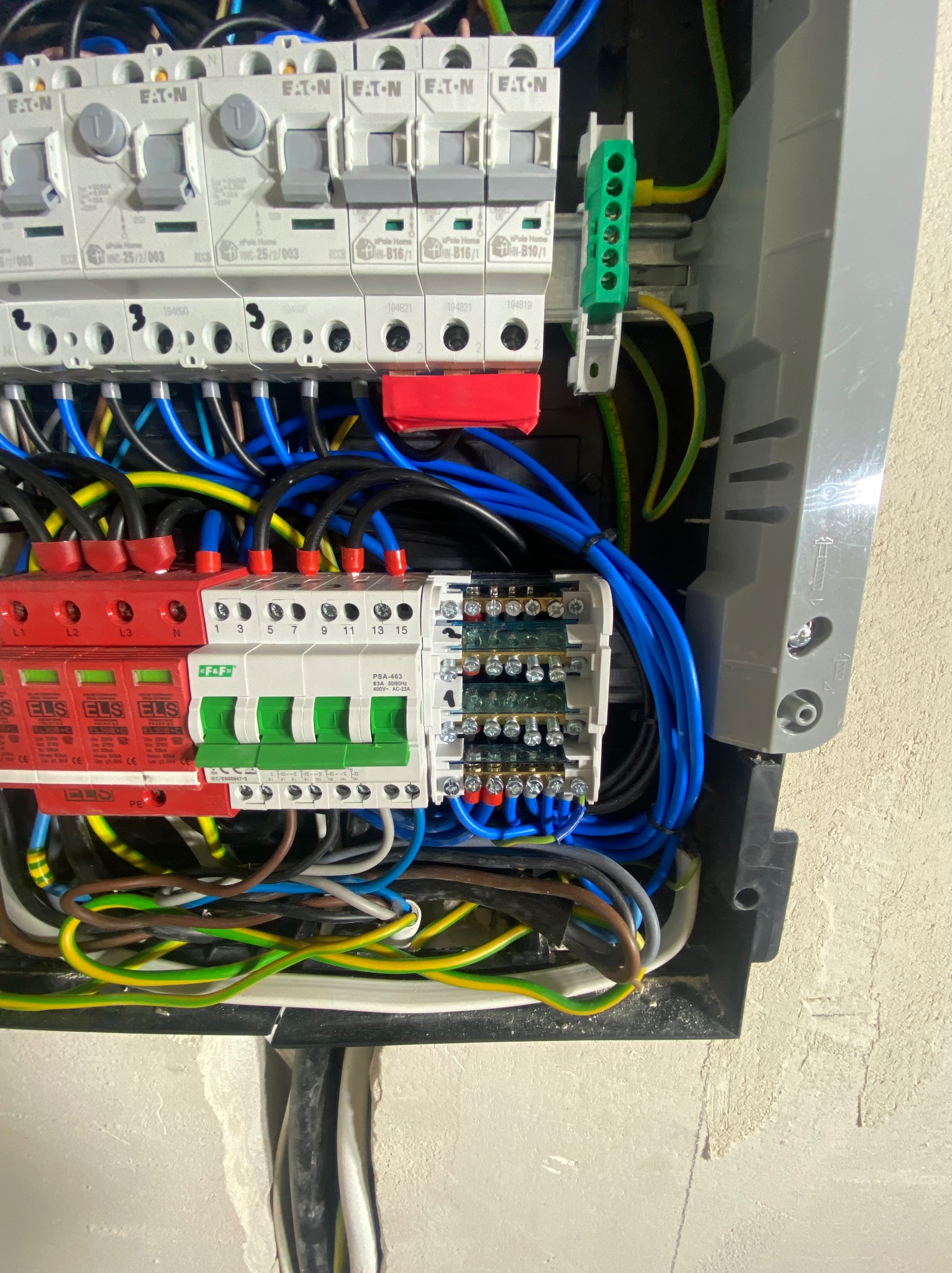 Rozdzielnica elektryczna z zabezpieczeniami przepięciowymi i różnicowoprądowymi, widoczne przewody w kolorach niebieskim, żółto-zielonym i czarnym.