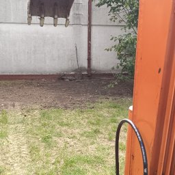 BODD-KOP - Prace ziemne w Pabianicach: łyżka koparki nad przygotowanym terenem pod instalacje, widoczna łopata. Wykopy pod szambo lub oczyszczalnię.