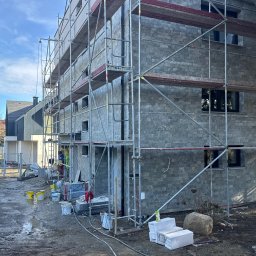 Elewacje z klasą - Montaż elewacji z kamienia na budynku wielorodzinnym w Krakowie. Widoczne rusztowania, materiały budowlane i pracownicy w trakcie pracy. Elewacja w odcieniach szarości.