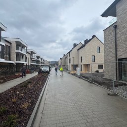 Elewacje z klasą - Nowoczesne osiedle domów w zabudowie szeregowej z elewacją z cegły klinkierowej, widok z perspektywy ulicy w pochmurny dzień. Część domów w trakcie wykończenia.
