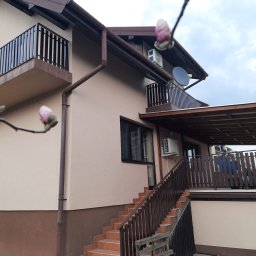 Elewacje z klasą - Dwukondygnacyjny dom z beżową elewacją i brązowymi akcentami, balkonami z balustradami i schodami zewnętrznymi, uchwycony w pochmurny dzień z kwitnącą magnolią na pierwszym planie.