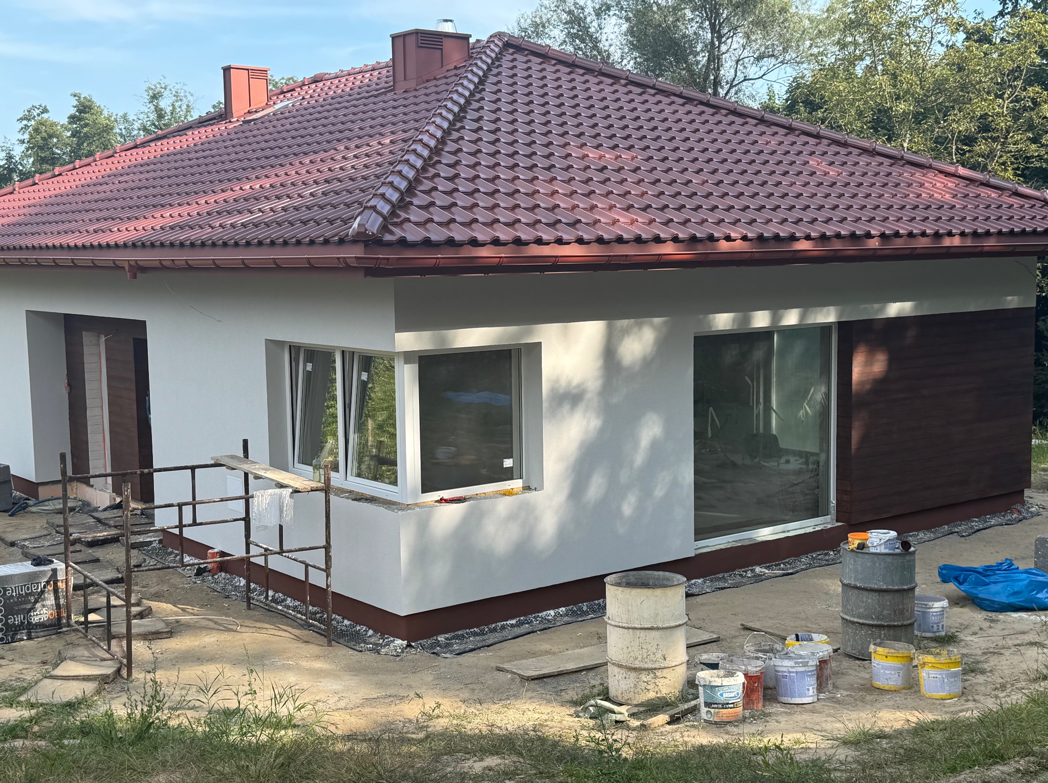 Elewacja domu jednorodzinnego w trakcie prac wykończeniowych, widoczne farby i rusztowania. Usługi elewacyjne w Krakowie.