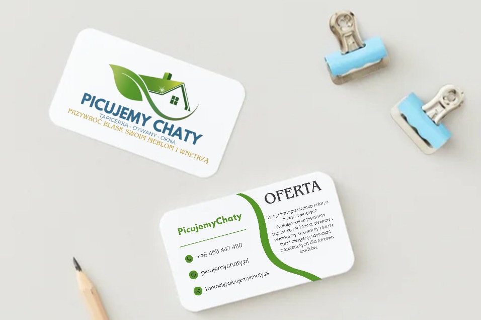 Dwie wizytówki z logo firmy 'Picujemy Chaty' obok ołówka i spinaczy biurowych. Grafika w odcieniach bieli i zieleni, z motywem domu i liścia. Minimalistyczny design.