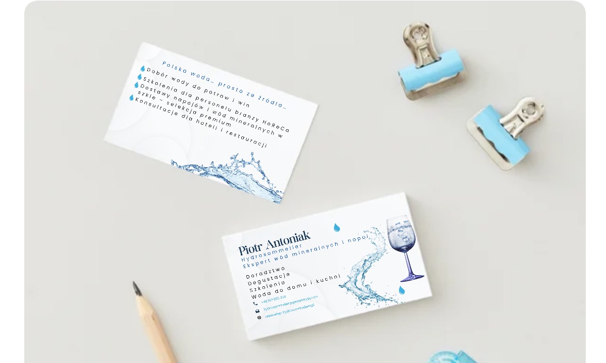 Dwie wizytówki z motywem wody, spinacze i ołówek na jasnym tle. Wizytówki z informacjami o doborze wody, szkoleniach i konsultacjach dla branży HoReCa.