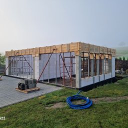 Firma Remontoo Budowlana - Budowa domu jednorodzinnego w trakcie realizacji: widoczne ściany z bloczków, szalunki na stropie i rusztowania. W tle zielony krajobraz.