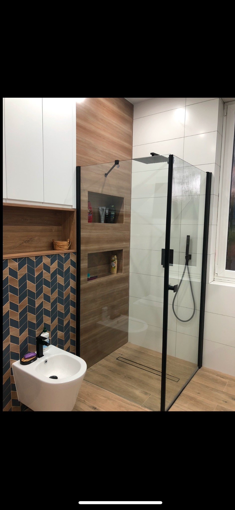 Nowoczesna łazienka z kabiną typu walk-in, drewnopodobne płytki, białe szafki i bidet. Uwagę przyciągają chevronowe płytki na ścianie.