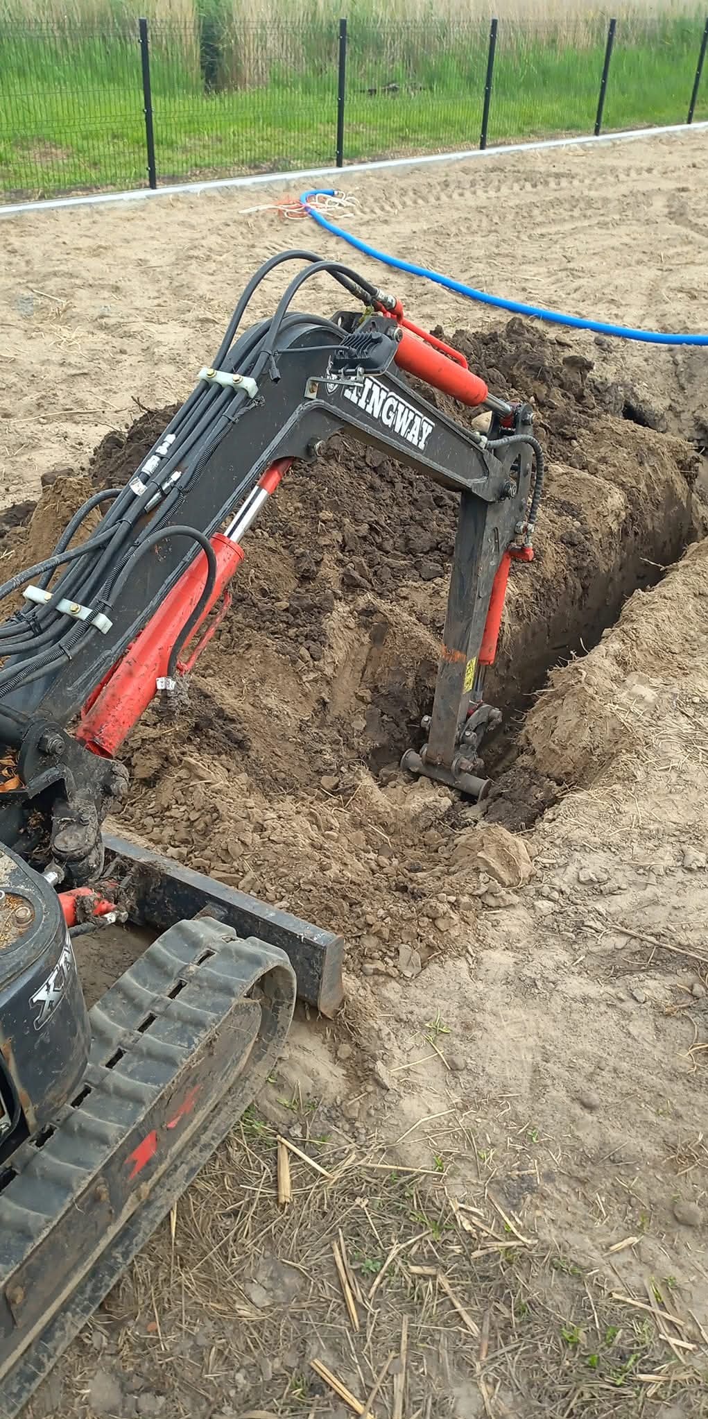 Mini koparka Kingway w trakcie prac ziemnych w Golina. Wykop pod instalacje, widoczne przewody. Sprzęt budowlany na placu budowy.