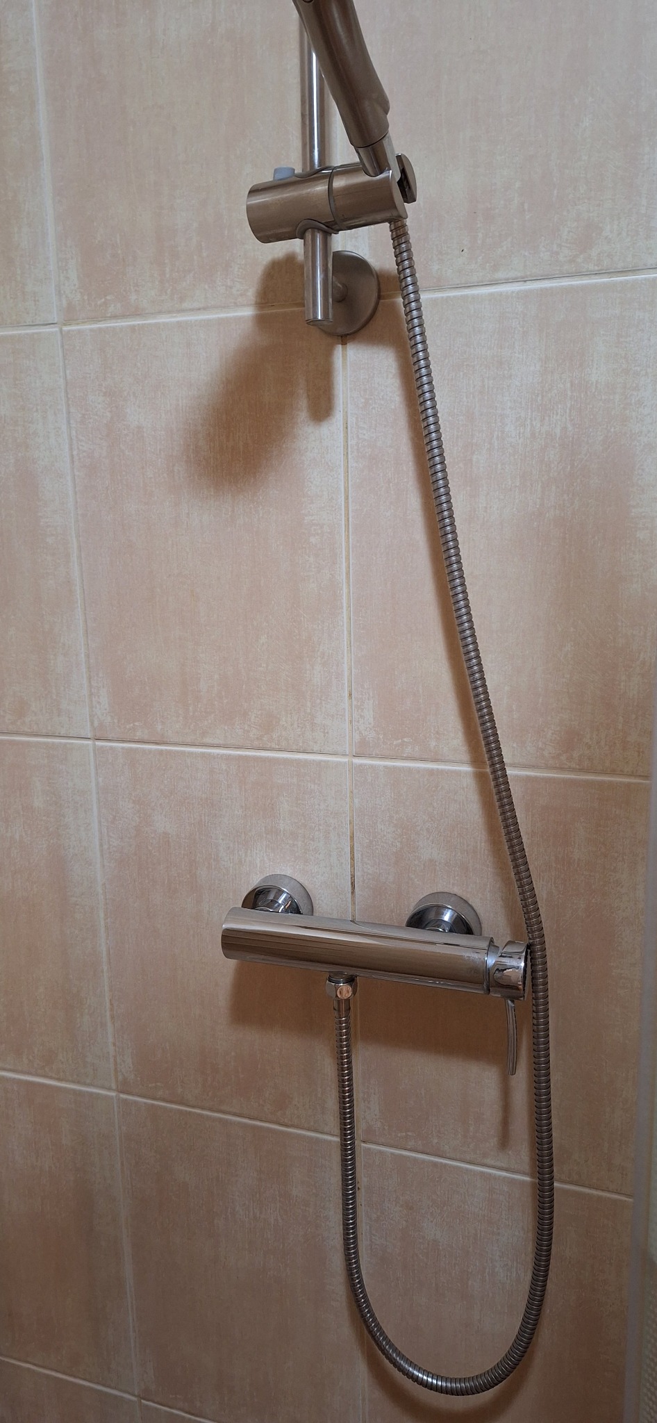 Bateria prysznicowa z deszczownicą na beżowych płytkach. Chromowana armatura łazienkowa po czyszczeniu, widoczne detale wykończenia.